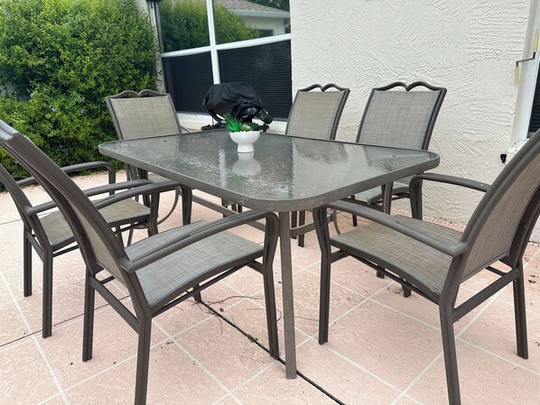 An outdoor patio with a glass-top table surrounded by four chairs.