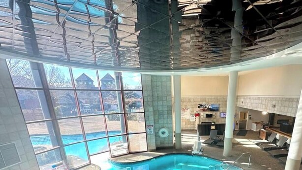 Une piscine intérieure avec des parois en verre transparent, un jacuzzi et une vue sur un bâtiment à l’extérieur.