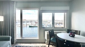 Une chambre d’hôtel moderne dotée d’une grande fenêtre donnant sur un port et sur le paysage urbain.