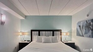 Une chambre d’hôtel avec un grand lit, deux tables de chevet avec des lampes, un mur bleu clair et un tableau encadré accroché au mur.