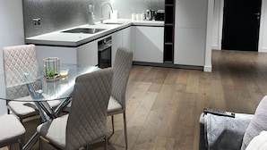 A modern kitchen with a glass dining table, grey upholstered chairs, and a built-in oven. - Stylish 1-bed Apartment in London (London)
