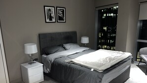 A modern bedroom with a large bed, two bedside tables with lamps, a grey headboard, and two framed pictures on the wall. - Stylish 1-bed Apartment in London (London)