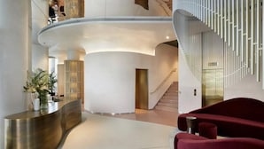 A modern lobby with a curved reception desk, a staircase, and a red seating area. - Stylish 1-bed Apartment in London (London)