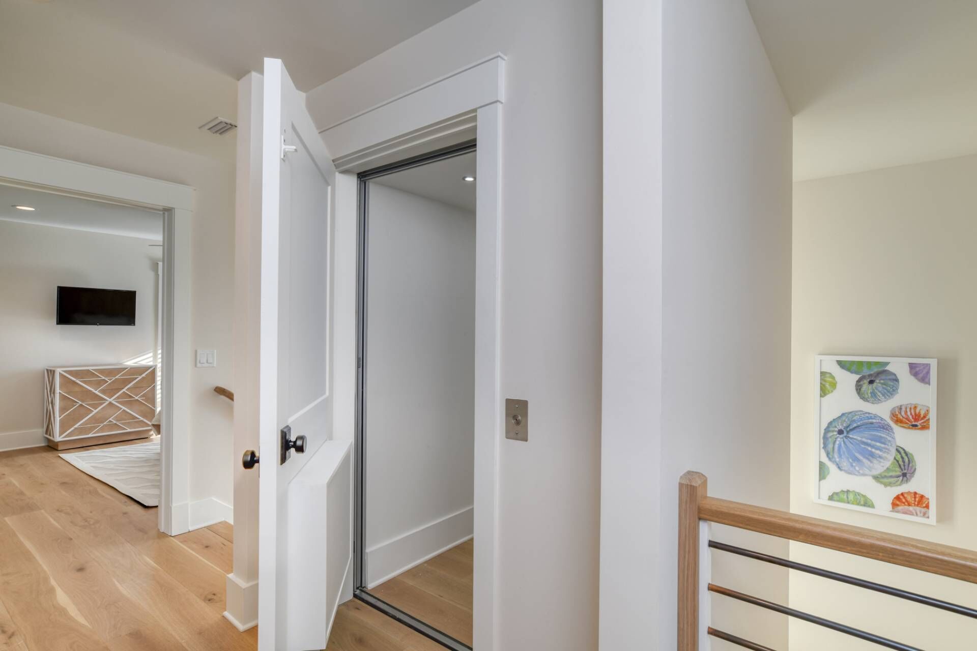 A modern interior with a white door, a wooden floor, and a framed artwork on the wall.