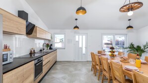 A modern kitchen with wooden cabinets, a black countertop, and a dining area with wooden chairs and a table. - Villa Berg II (Istria - Valbandon) (Valbandon)