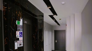Un pasillo con suelo de mármol, una puerta de ascensor de vidrio y una puerta de ascensor oscura.