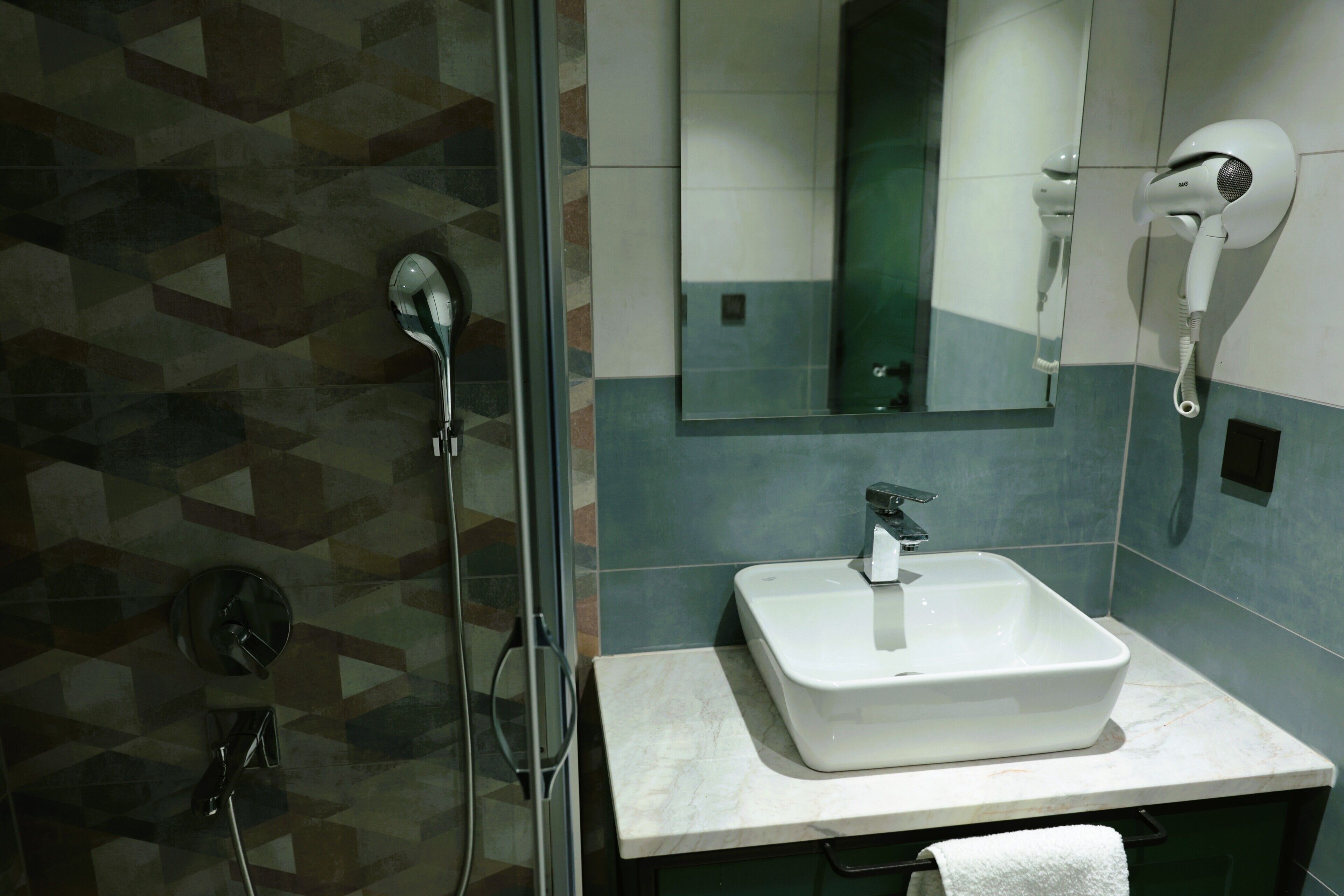 A bathroom with a glass shower enclosure, a white sink, and a hairdryer mounted on the wall.