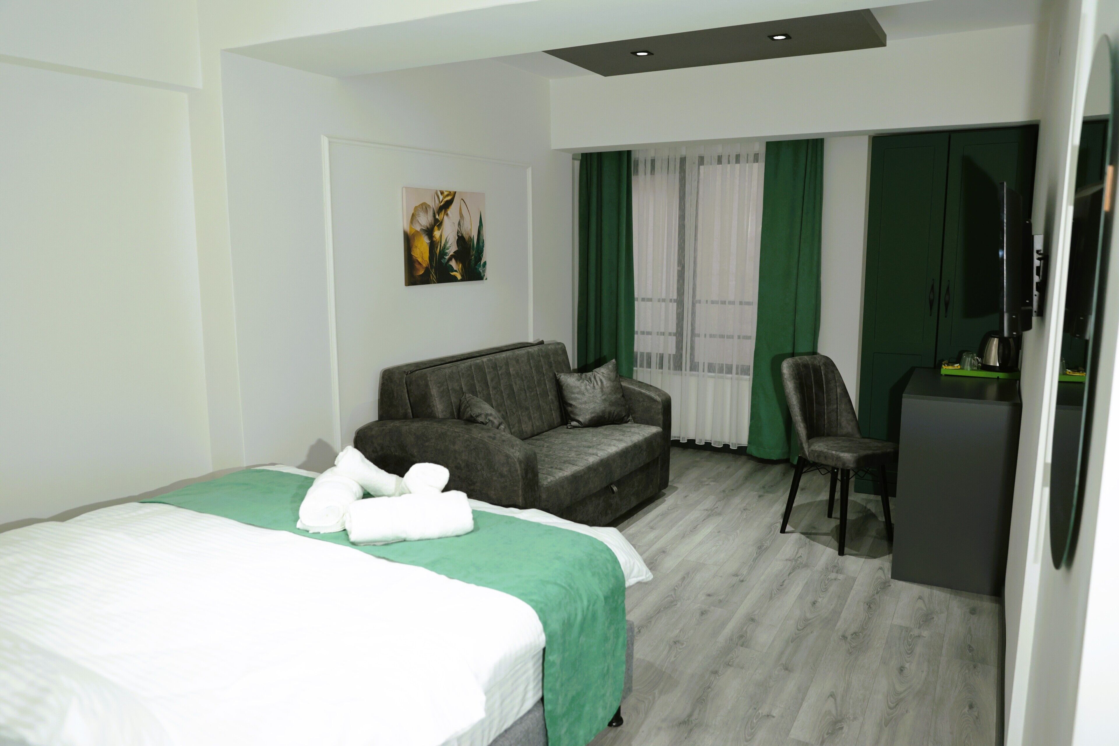 A hotel room with a bed, a sofa, a chair, a desk, and a television.