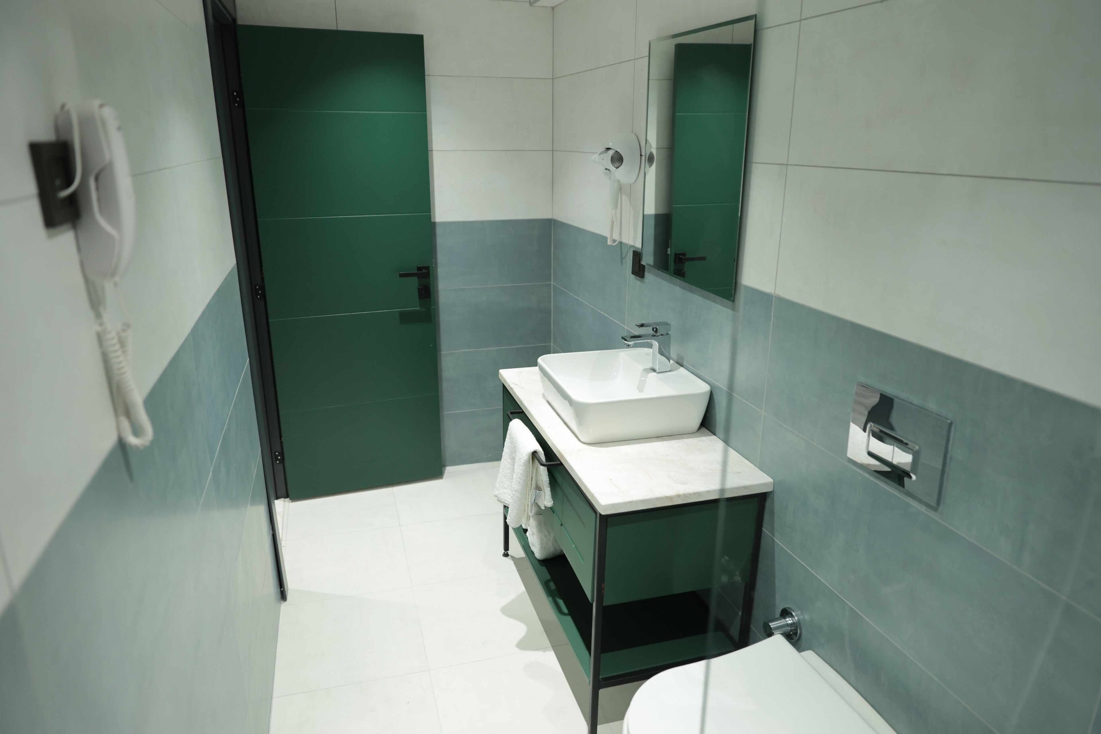 Un baño moderno con un lavabo blanco, un espejo y una puerta verde.