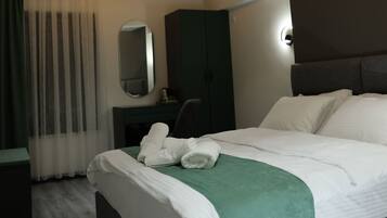 Ett modernt hotellrum med en stor säng, en grön pläd, en mörk sänggavel, en spegel och en mörk garderob.