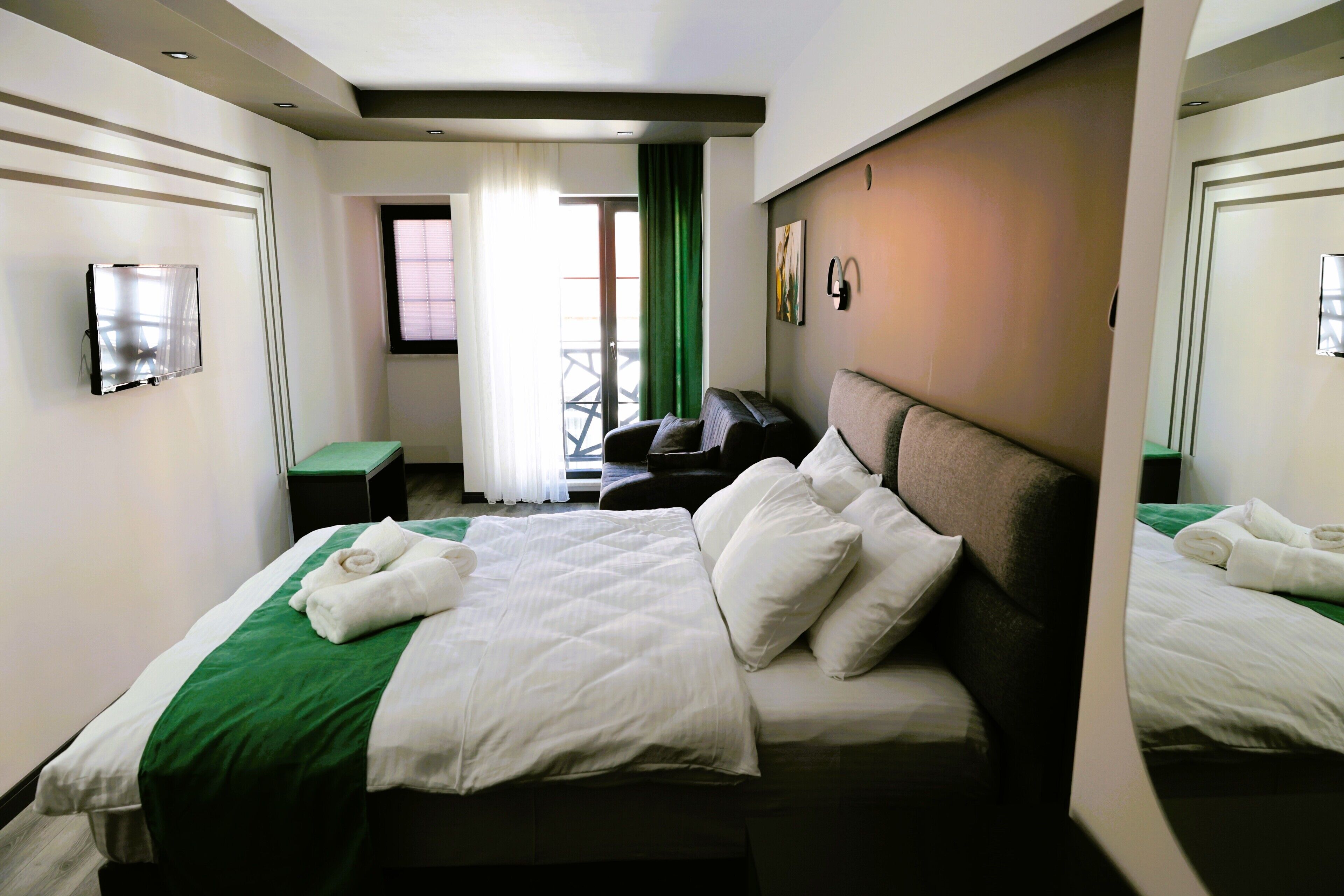 A hotel room with a bed, a bedside table, a mirror, and a window with curtains.