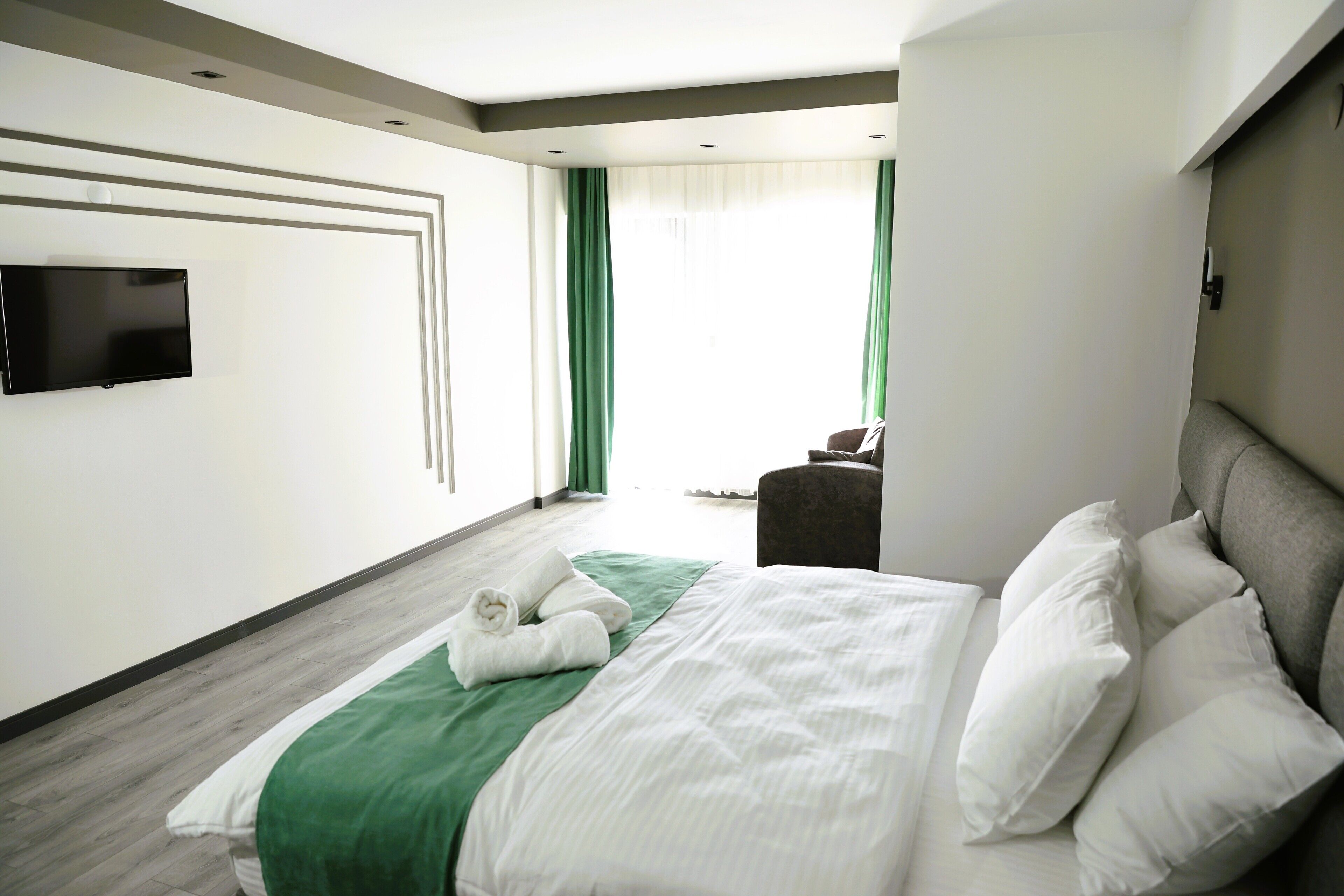 A hotel room with a large bed, a flat-screen TV mounted on the wall, and a view of the outdoors through a window.