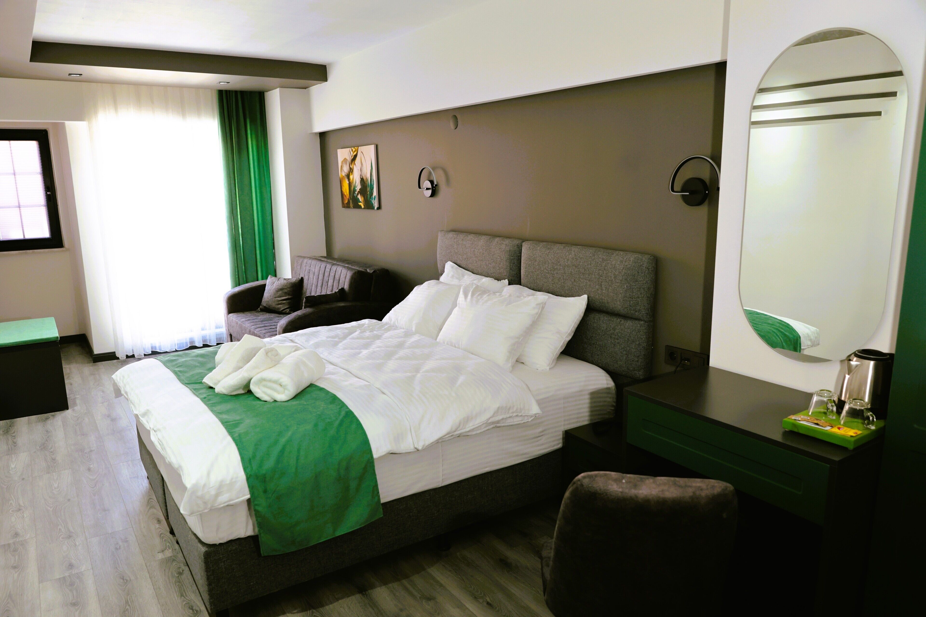 Una habitación de hotel con cama, escritorio, silla, espejo y ventana con cortinas.