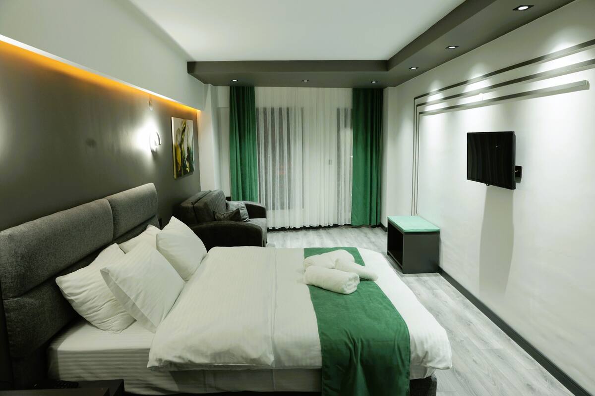 Een moderne hotelkamer met een groot bed, een bank, een klein tafeltje en een aan de muur bevestigde televisie.