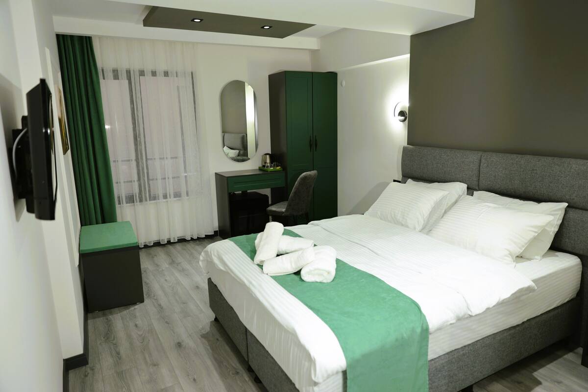 Een hotelkamer met een groot bed, een bureau, een stoel, een garderobe en een spiegel.