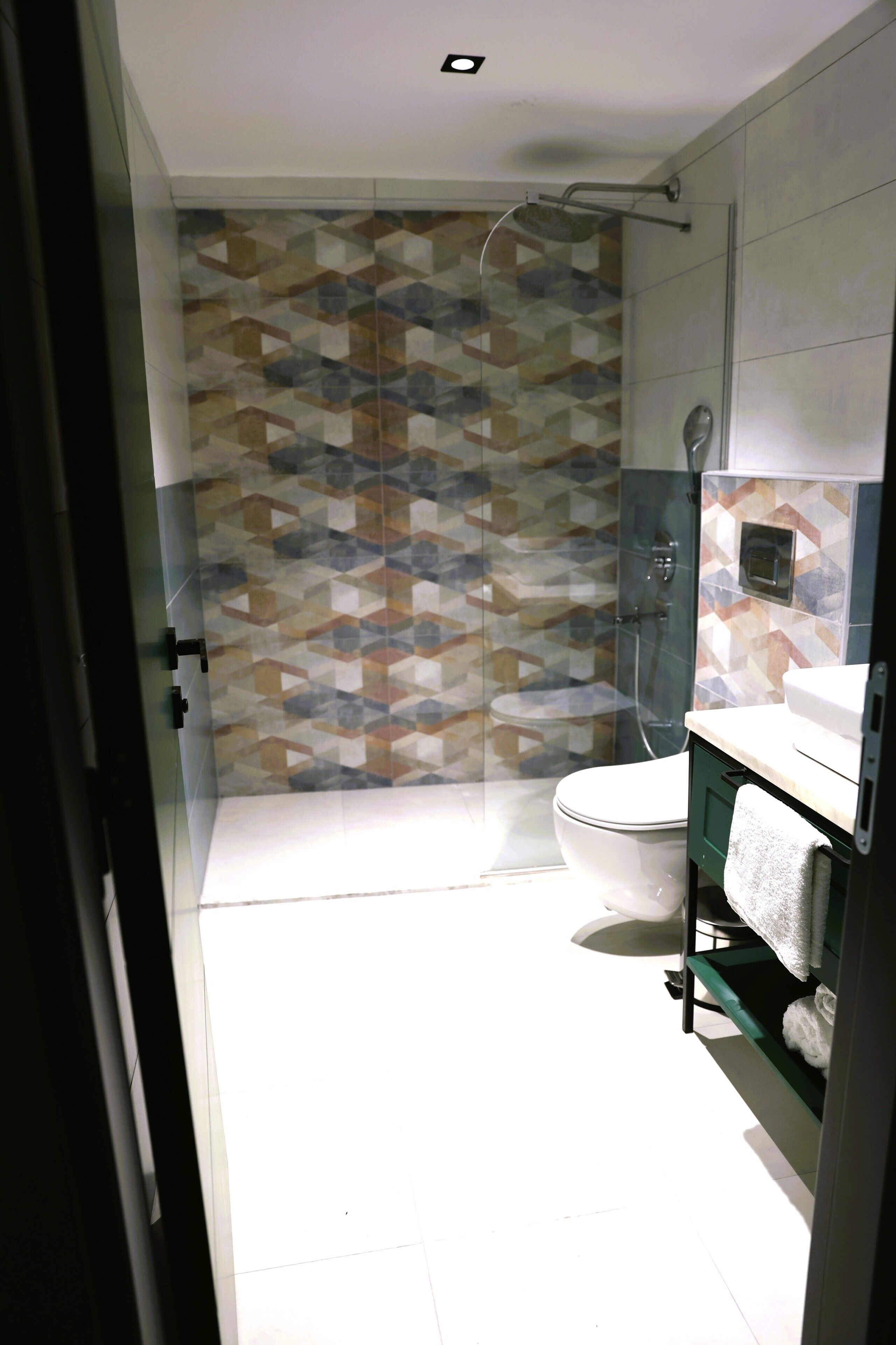Une salle de bain avec un mur recouvert de carreaux à motifs, des toilettes, un espace douche et un porte-serviettes avec des serviettes.