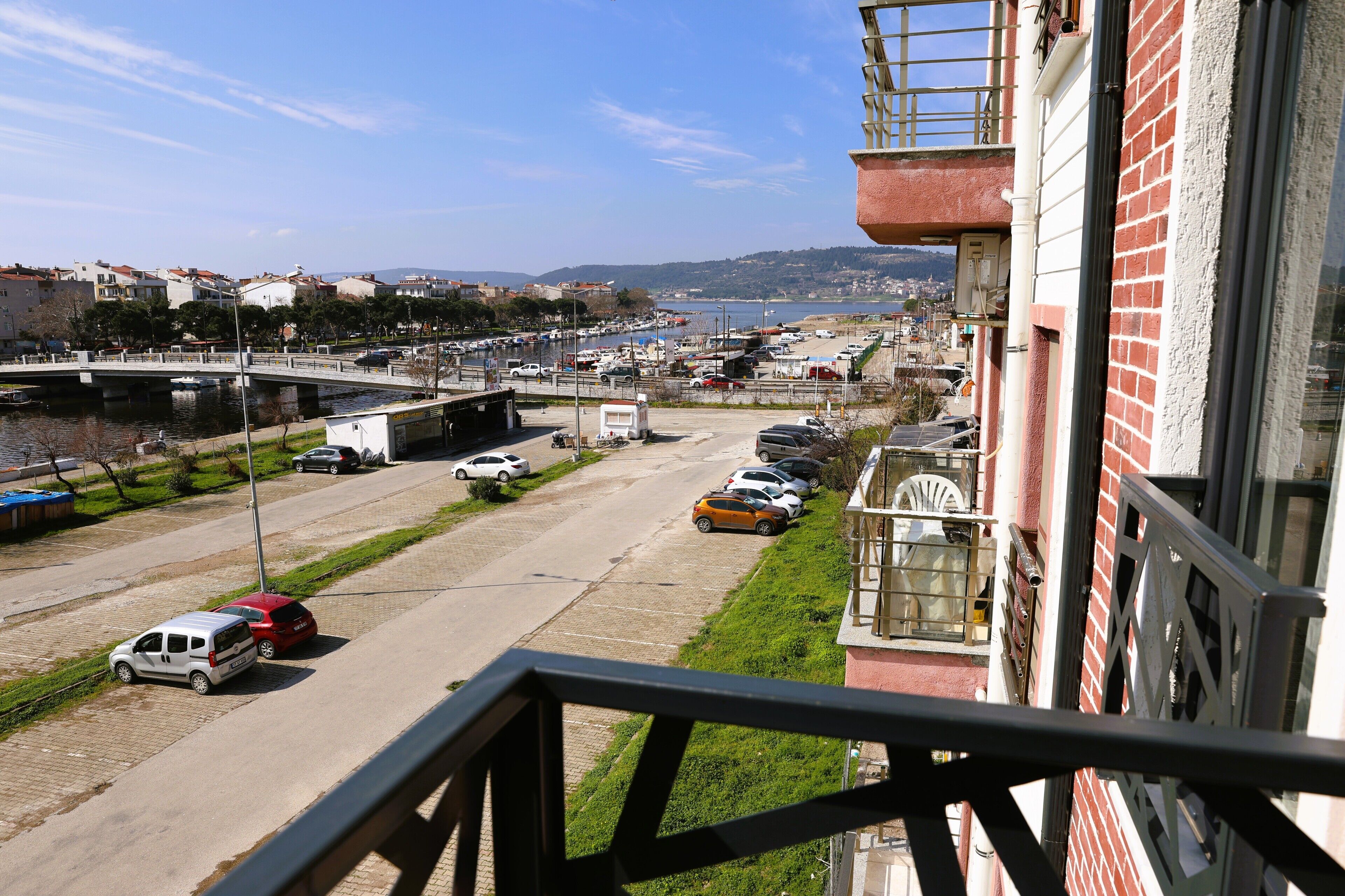 A view from a balcony overlooking a street with parked cars, a bridge, and a body of water in the distance.