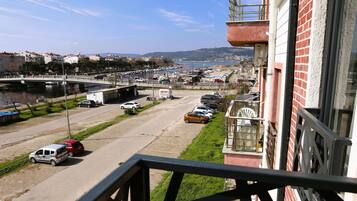 A view from a balcony overlooking a street with parked cars, a bridge, and a body of water in the distance.