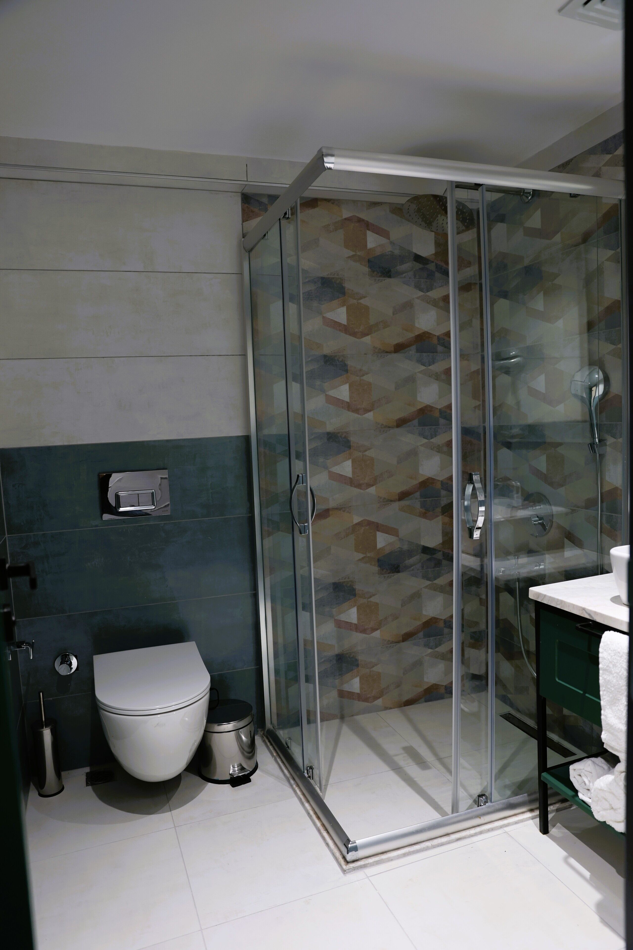 A modern bathroom with a glass shower enclosure, a toilet, and a sink with a green vanity.