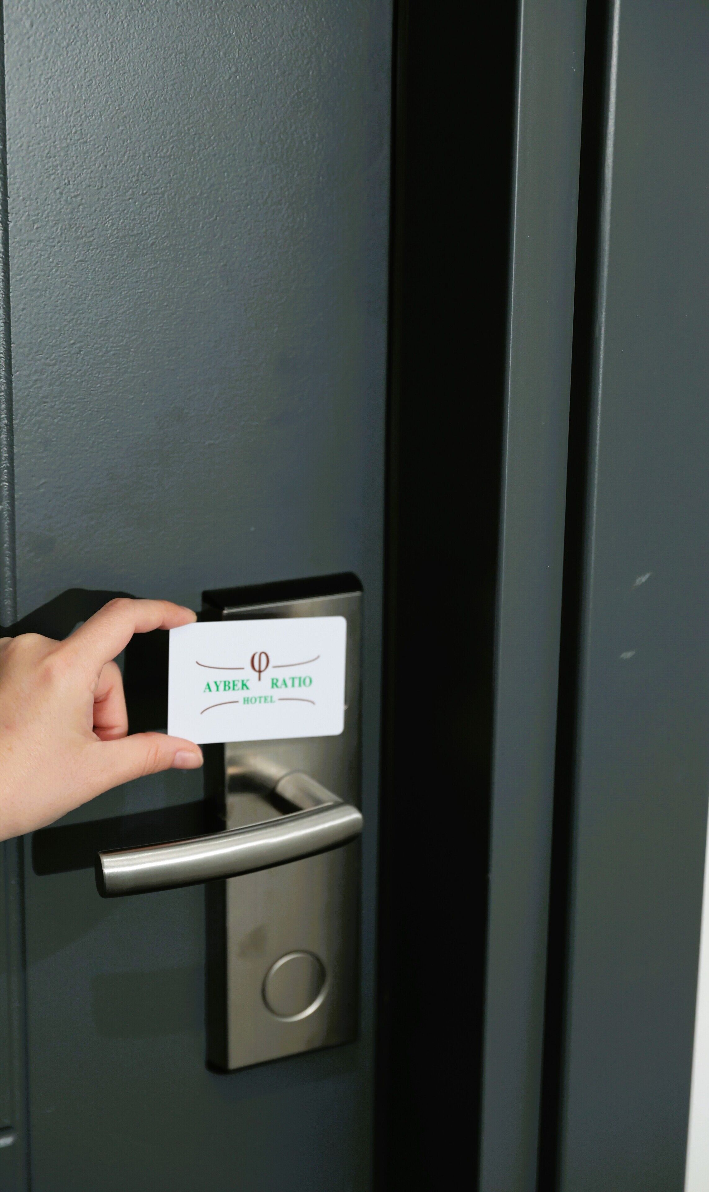 A hand holding a card with "AYBEK HOTEL" written on it, inserted into a door lock mechanism.