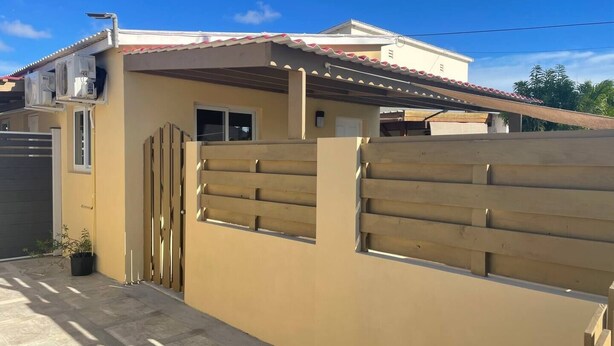 A residential building with a beige exterior, a red-tiled roof, and a wooden fence. - Taminaka Condominium Comfortable II (Oranjestad)