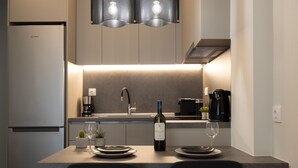 A compact kitchen with a built-in refrigerator, a coffee maker, and a wine bottle on the counter. - Modern Apt. ideal for families/couples,10 mins from Thessaloniki's vibrant heart (Thessaloniki)