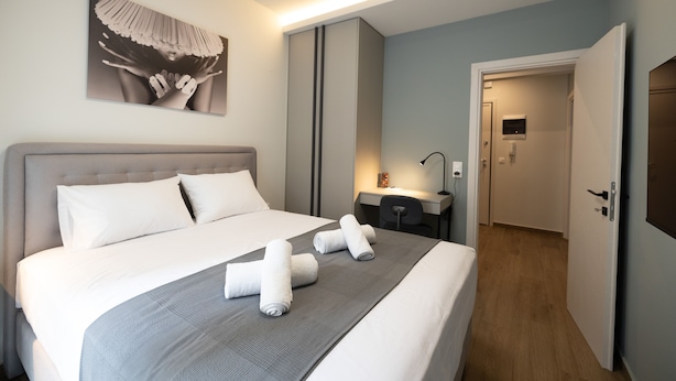 A neatly made bed with white linens and gray bedding, a bedside table with a lamp, and a painting on the wall. - Modern Apt. ideal for families/couples,10 mins from Thessaloniki's vibrant heart (Thessaloniki)