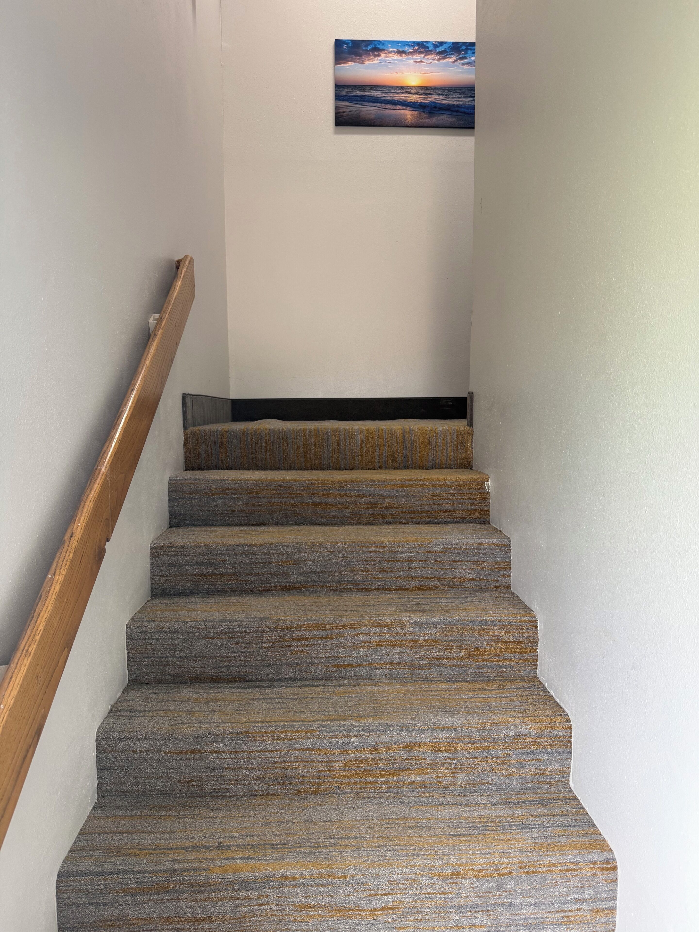 A staircase with a wooden handrail and carpeted steps leading to a landing.