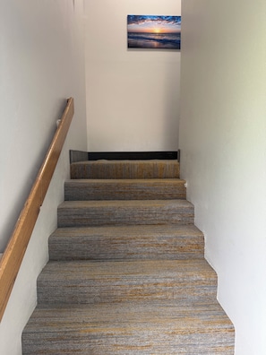 A staircase with a wooden handrail and carpeted steps leading to a landing.