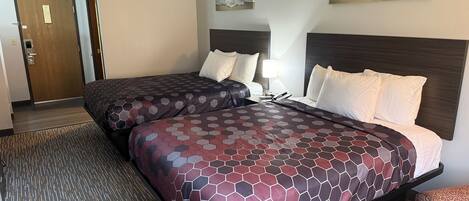 A hotel room with two beds, a wooden door, and two wall-mounted paintings.