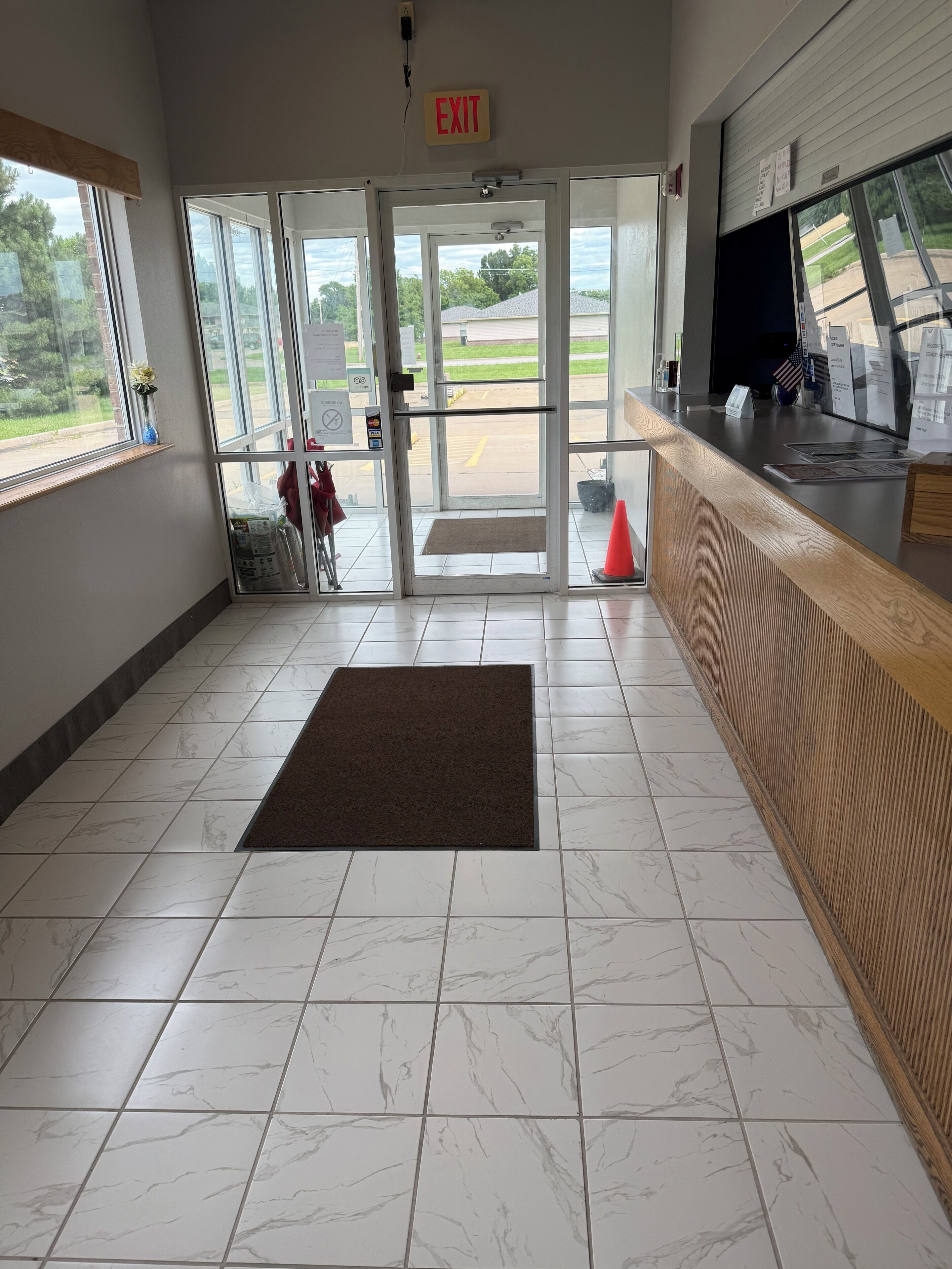Vestíbulo de hotel con mostrador de recepción, señal de salida, rampa y vistas al exterior.