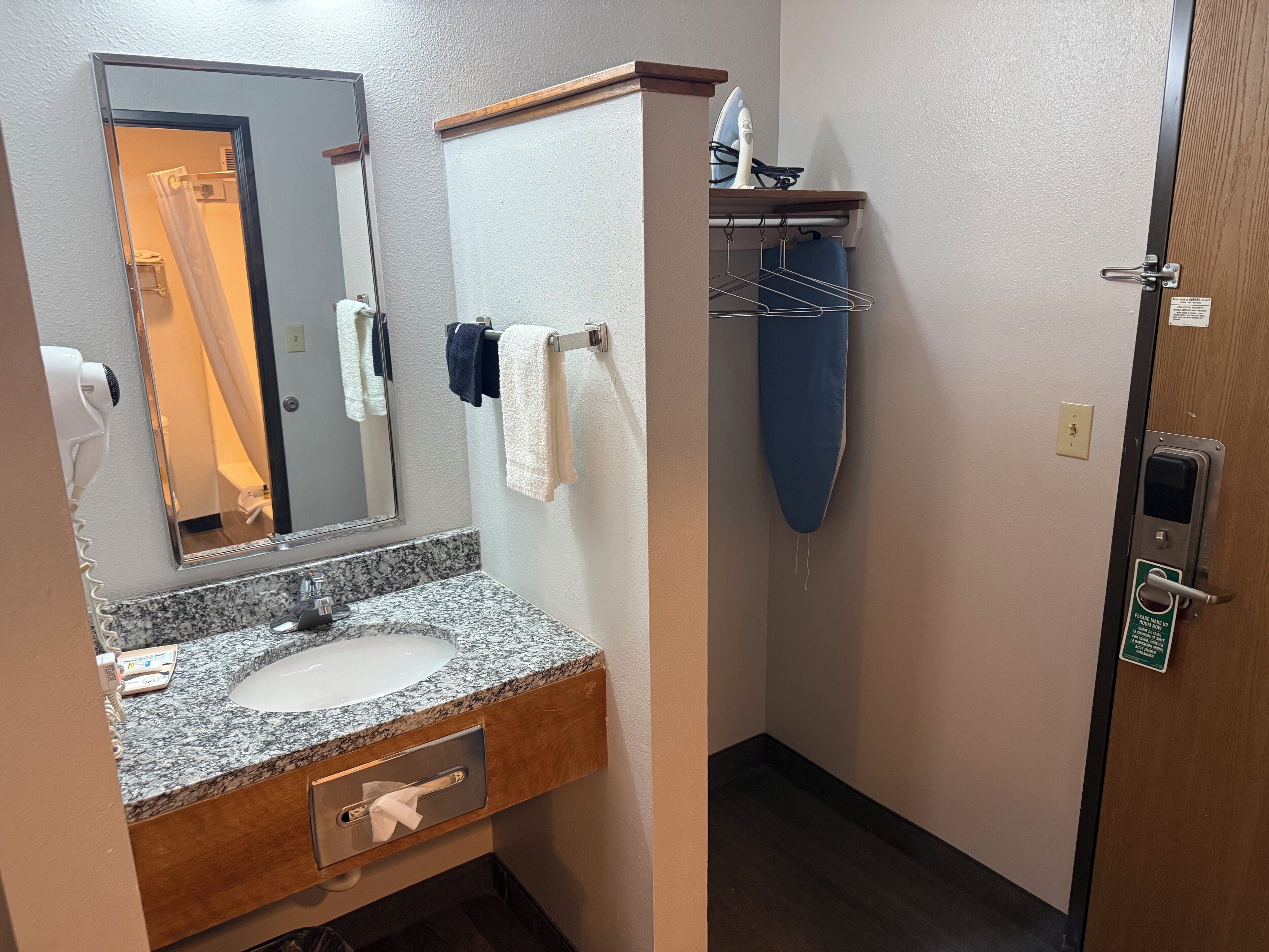Une salle de bain avec un lavabo doté d’un plan de travail en granit, un miroir, un porte-serviettes avec plusieurs serviettes, un sèche-cheveux et une porte avec une serrure.