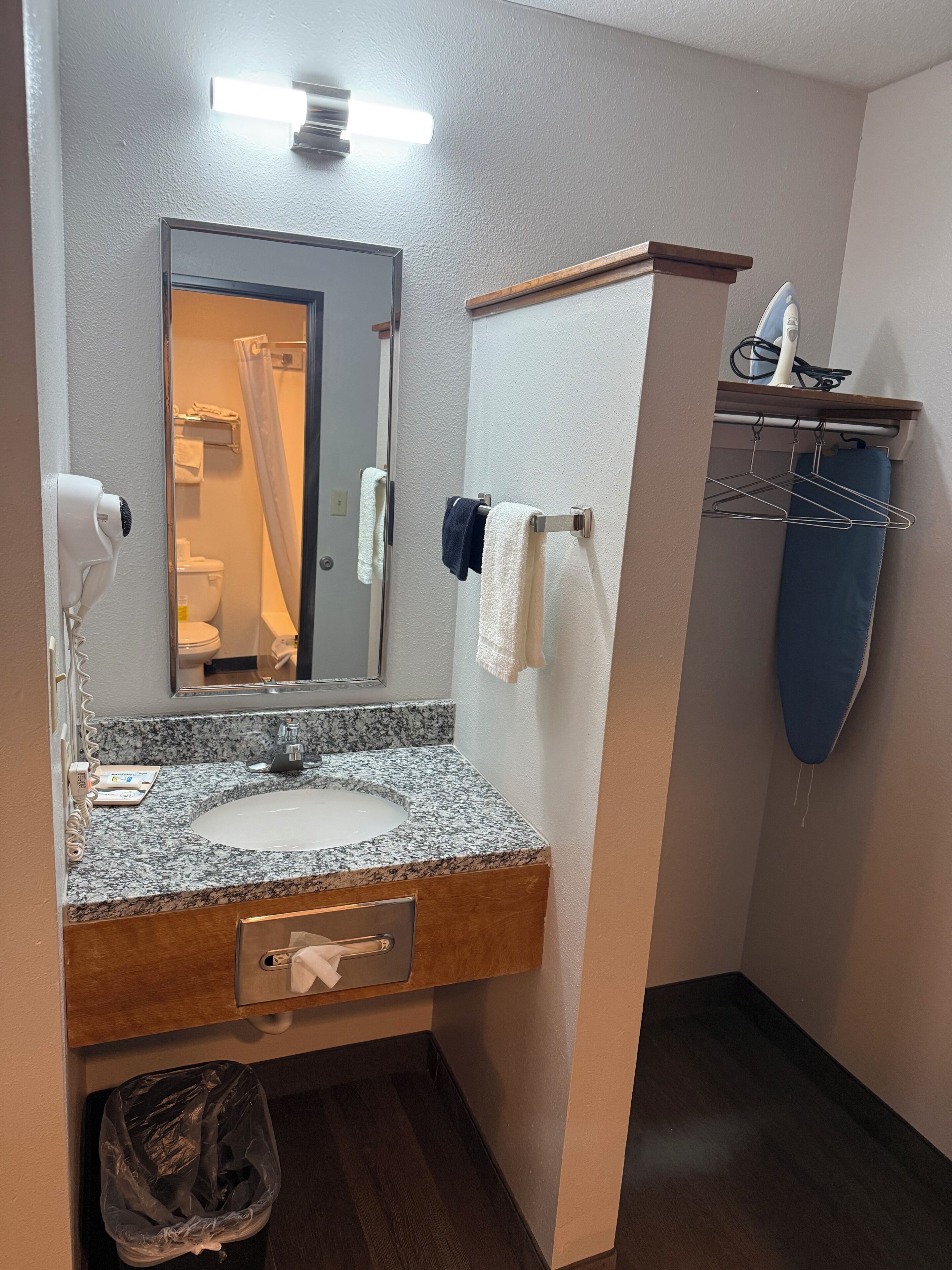 Un baño con lavabo de encimera de granito, espejo, toallero, cortina de ducha y secador de pelo.