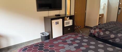 A hotel room with a bed, a TV, a desk with a microwave, a trash bin, and a door.
