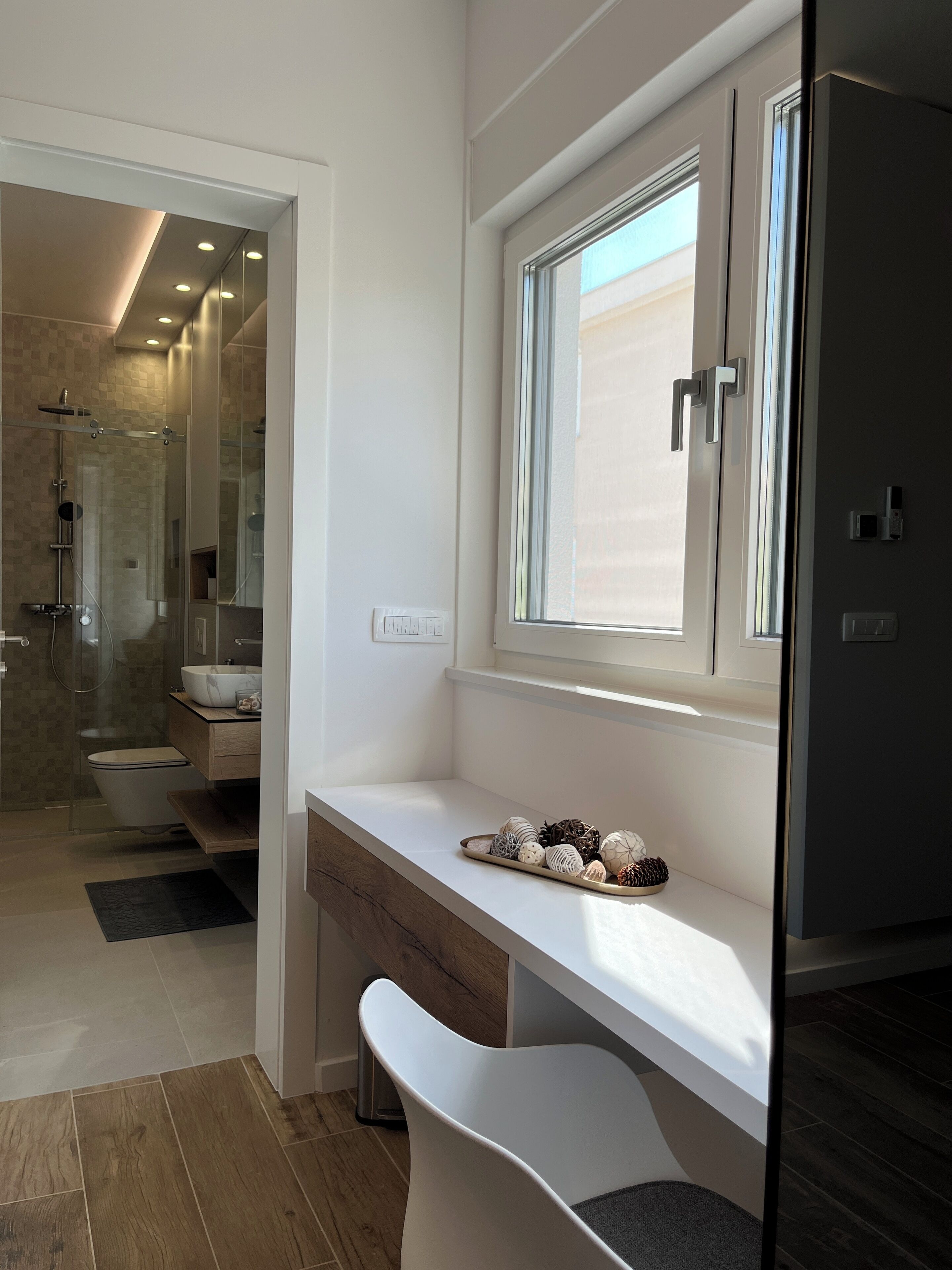 Un bagno moderno con doccia, servizi igienici e lavandino. Sopra il lavandino c'è una finestra e al muro un grande specchio.