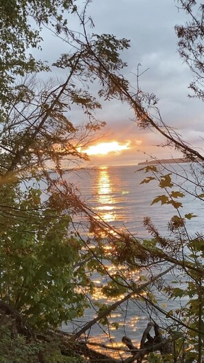 A sunset over a calm body of water with reflections of the sky, surrounded by trees. - Lake Superior shoreline, wilderness camping. (L'Anse)
