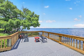 A wooden deck with a railing overlooking a body of water, featuring two metal chairs and a small table.