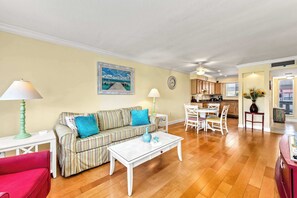 A living room with a striped sofa, a red chair, a white coffee table, and a dining area with a white table and chairs. - Pickleball • Private Beach Access • Largest Pool (Bradenton Beach)