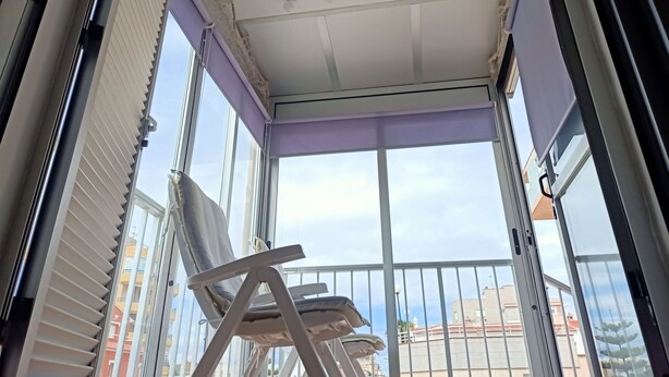 A balcony with a white ceiling, a white ceiling fan, and a view of buildings in the background. - Sol y Playa Oliva (VC)