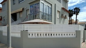 A modern building with a balcony, a covered outdoor seating area, and a gated entrance. - Sol y Playa Oliva (VC)