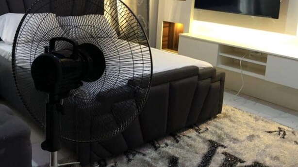 Une chambre moderne avec un grand lit, un ventilateur sur pied, une télévision et un panneau décoratif mural.