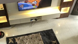 Un hall d’hôtel avec un téléviseur à écran plat diffusant un dessin animé, un pouf capitonné et un tapis noir orné de lettres dorées.