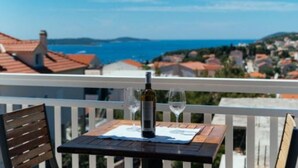 Un balcon avec une table dressée pour deux personnes, offrant une vue sur une ville côtière avec ses maisons et la mer.