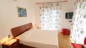 A bedroom with a bed, bedside tables, a lamp, a TV, and a red chair.