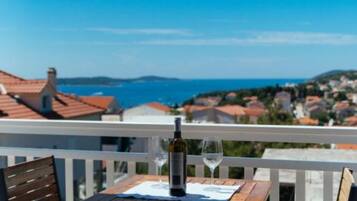 A balcony with a table set for two, overlooking a coastal town with houses and the sea.