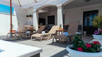 An outdoor patio with sun loungers, umbrellas, and potted plants.