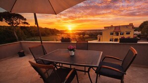 Eine Terrasse mit Tisch, Stühlen und einem Sonnenschirm, mit Blick auf einen Sonnenuntergang.