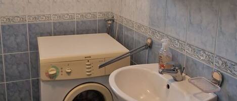 Une petite salle de bain équipée d’un lave-linge, d’un lavabo et d’un miroir.