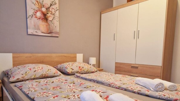 A double bed with floral bedding, a nightstand with a lamp, and a wardrobe with two doors. - Apartments Sunset - Two bedroom Apartment (Porec)