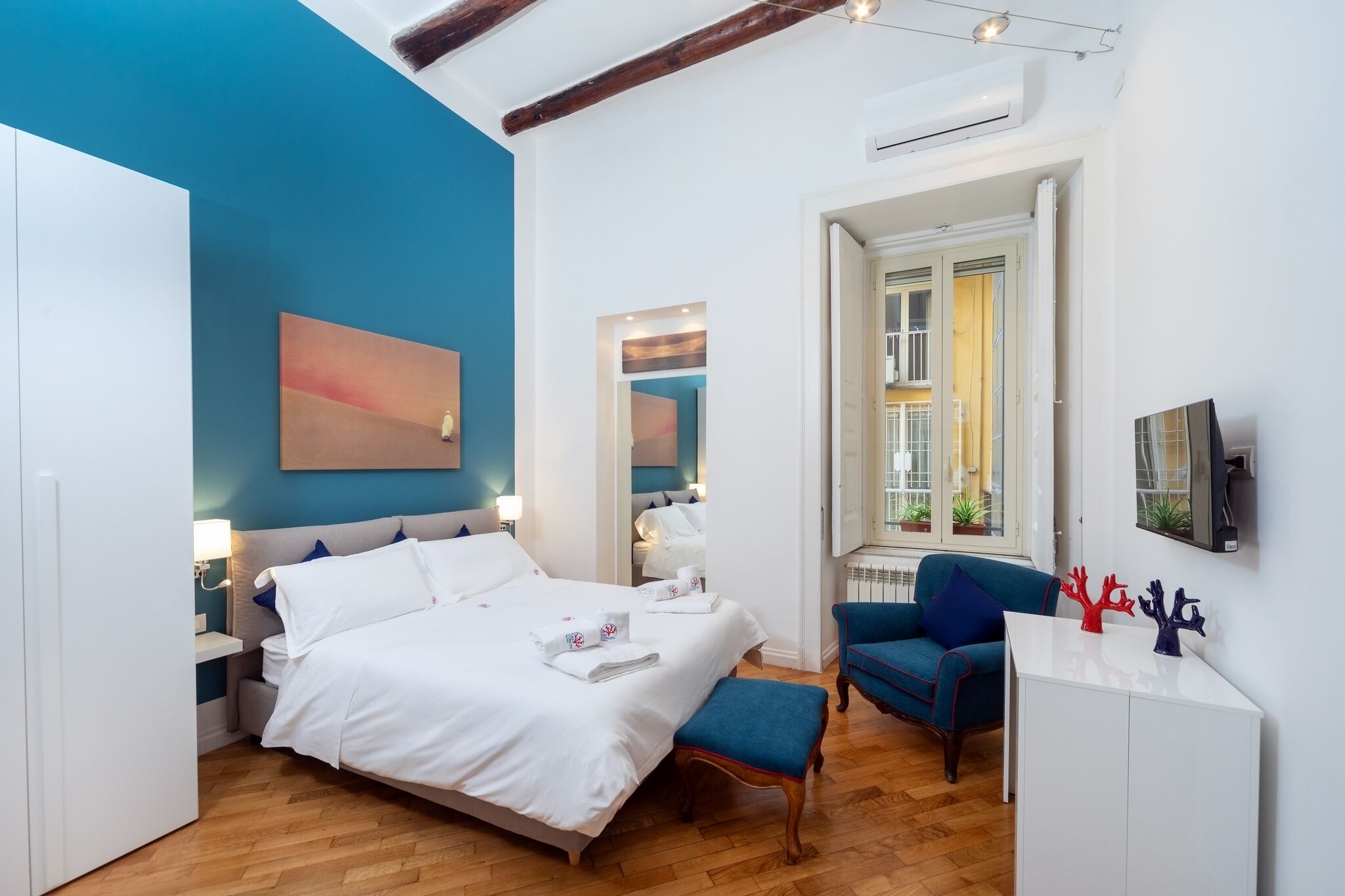 A modern bedroom with a large bed, a blue armchair, and a desk with decorative items.